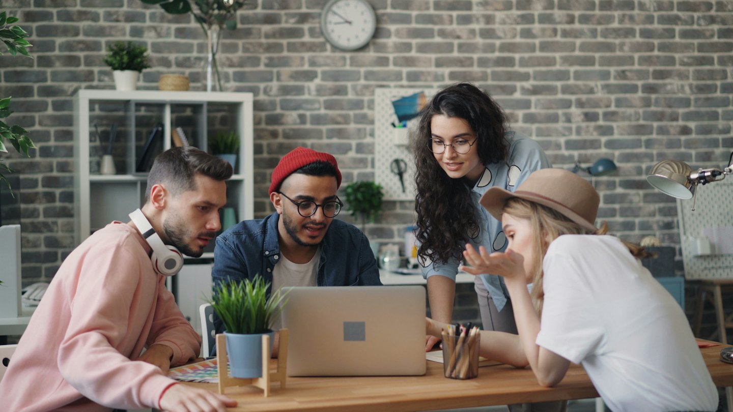 Diverse team collaborating on a laptop in a bright office.