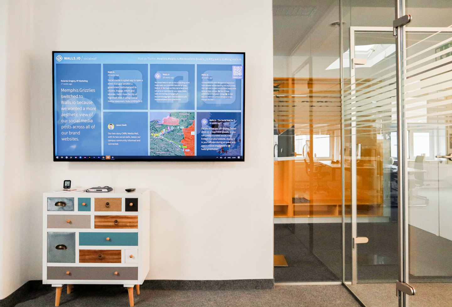 Modern office with large monitor showing social media feed and colorful dresser.